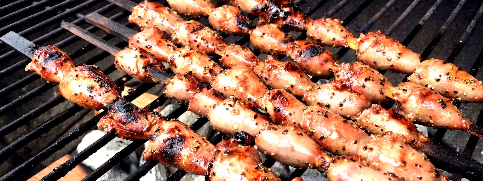 A imagem mostra espetinhos de coração de galinha sobre uma grelha.