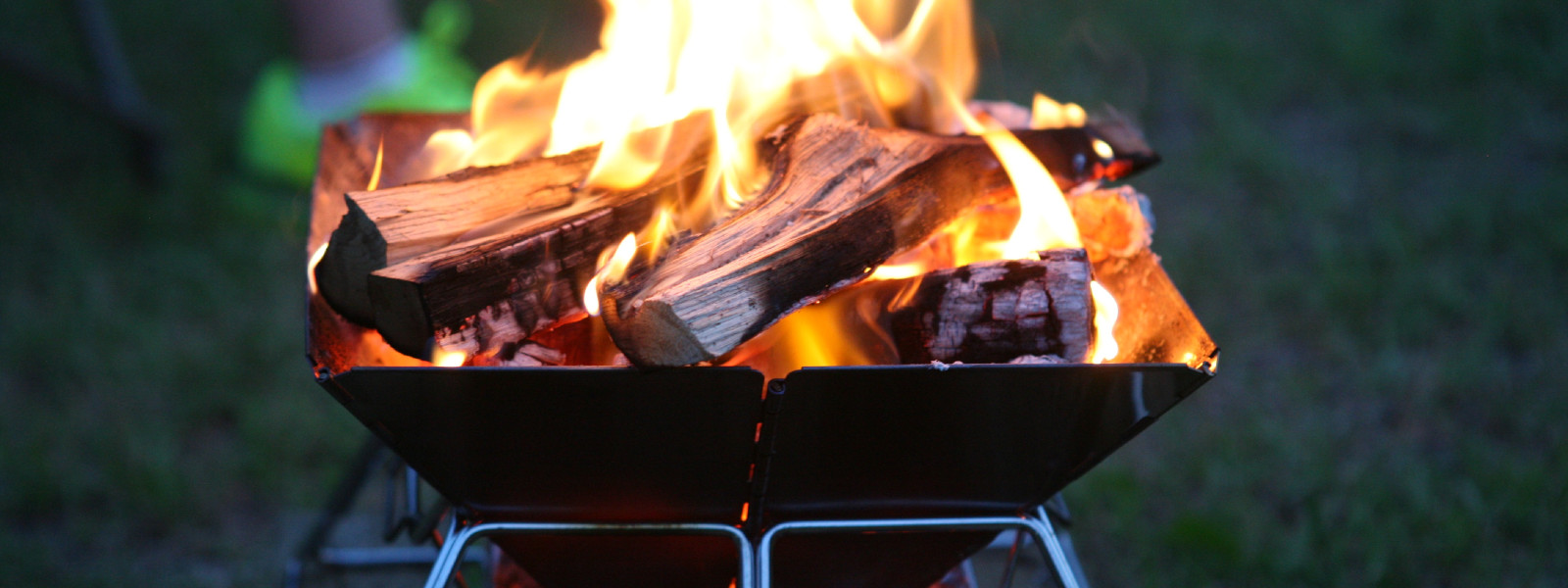 A imagem mostra uma churrasqueira portátil acesa na grama