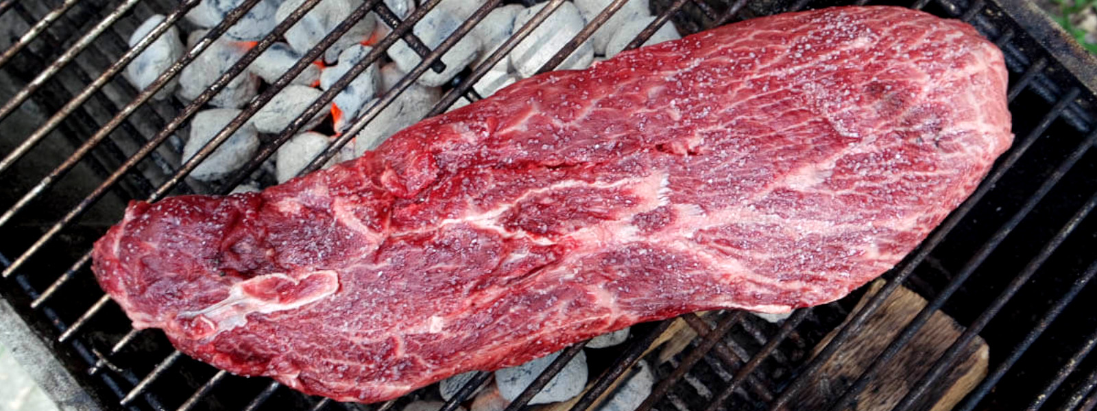 A imagem mostra uma peça de flat iron sobre uma grelha com briquetes.
