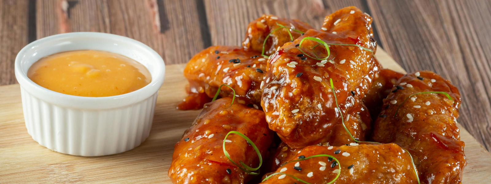 A imagem mostra uma tábua de corte com asinha de frango no forno em cima.