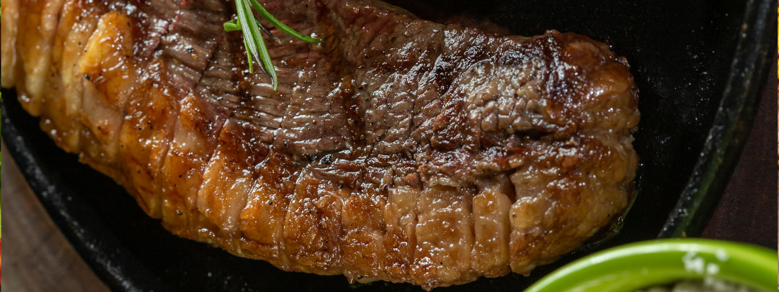 A imagem mostra uma picanha no churrasco sendo servida com uma folha de alecrim