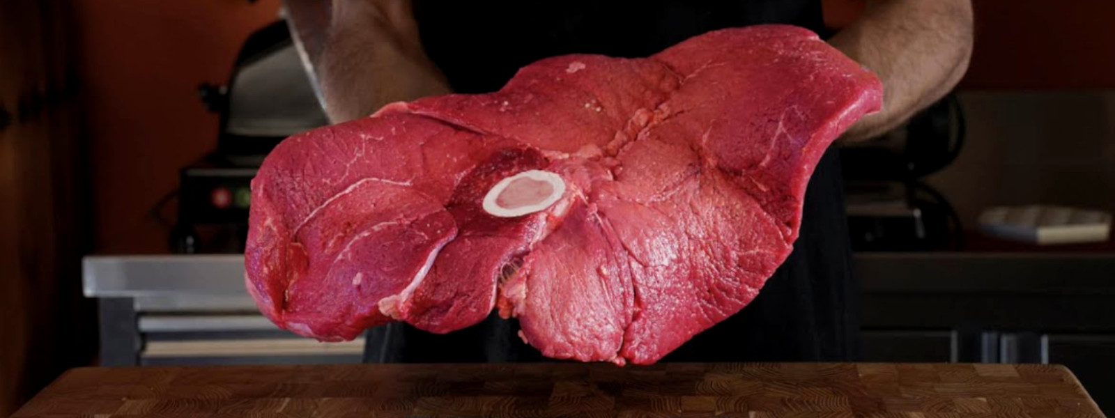 A imagem mostra um açougueiro segurando um bife do capitão