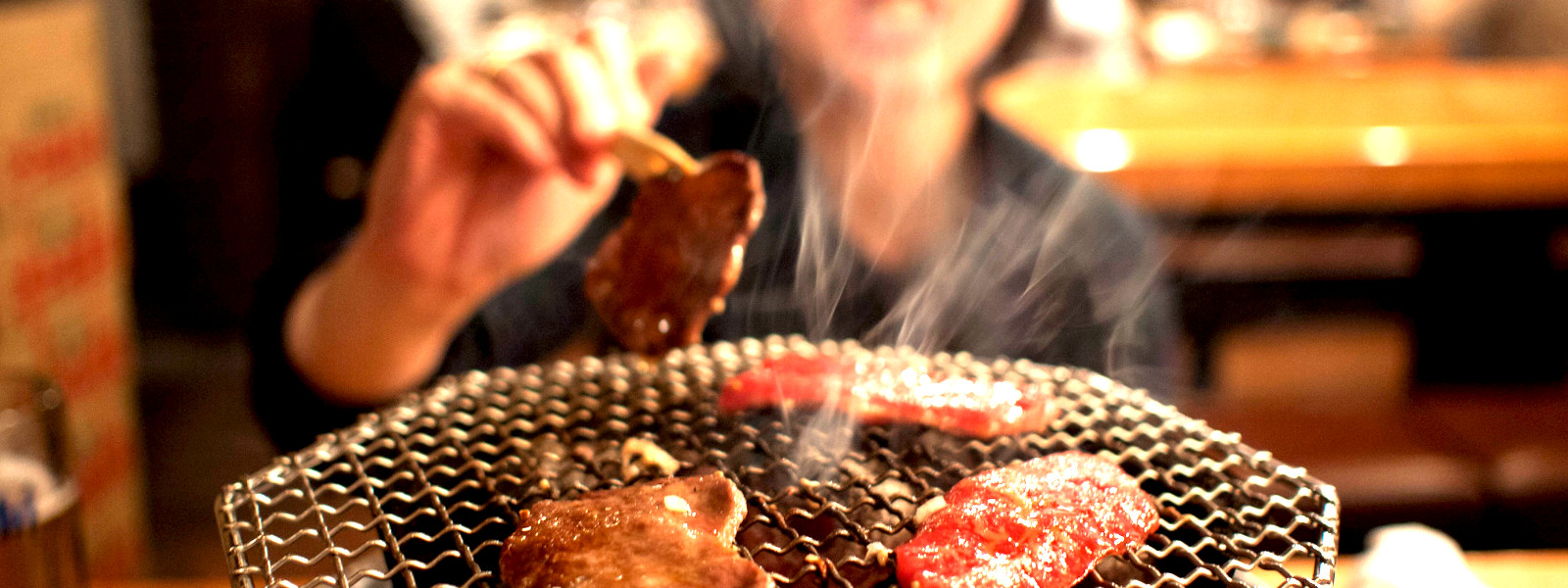 A imagem mostra uma mulher oriental comendo yakiniku, o churrasco japonês